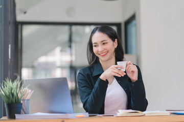 Happy young Indian businesswoman entrepreneur using a computer to work on the internet while sitting at her office desk.