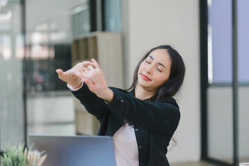 An attractive young Asian millennial businesswoman is stretching her arms during a break in the office.