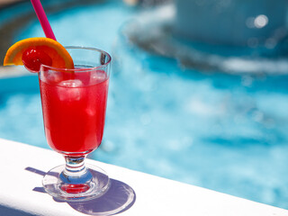 Glass of non alcoholic Pink panther cocktail on pool border at tropical resort