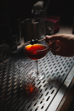 Bartender hand placing cherry garnish on top of Manhattan style craft cocktail on bar top.