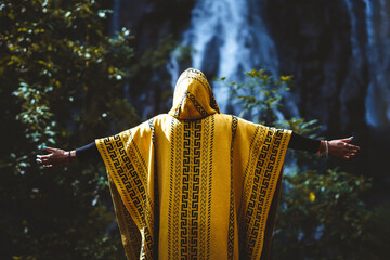 mujer por detrás con los brazos extendidos con una manta amarilla frente a la cascada del velo de novia en valle de bravo, méxico
