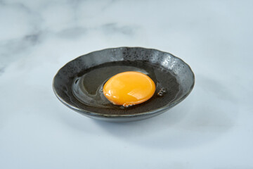 大理石の背景と黒い皿に入った生卵