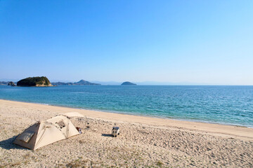 Fototapeta na wymiar トイプードルを連れて女子キャンプ　青い海・美しいビーチでのんびり島キャンプ　キャンプ料理や愛犬と休日を楽しむ女性　海の見えるキャンプ