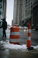 a snowy day in the city with cones on the street and person walking in background