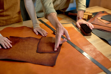 active craftsman shows to craftswoman where to cut leather, close up portrait, young people working with pieces of natural material