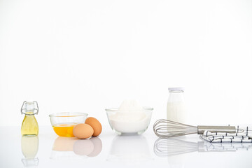 Baking ingredients on white reflect table over defocused white kitchen wall background.
