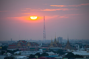.The red sun beside a huge signal tower in the heart of Bangkok..beautiful red sky at sunset. Temples and buildings in Bangkok background..