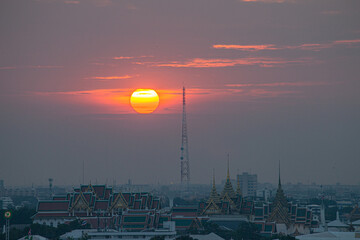 Obraz premium .The red sun beside a huge signal tower in the heart of Bangkok..beautiful red sky at sunset. Temples and buildings in Bangkok background..
