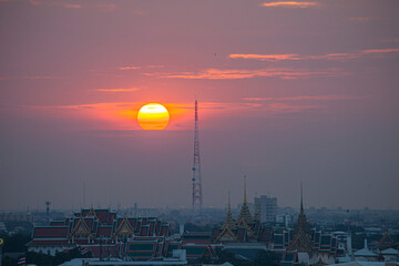 .The red sun beside a huge signal tower in the heart of Bangkok..beautiful red sky at sunset. Temples and buildings in Bangkok background..