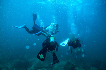 Fototapeta na wymiar Scuba Divers, silhouettes against sunburst, in the ocean beside coral reef