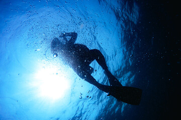Scuba Divers, silhouettes against sunburst, in the ocean beside coral reef
