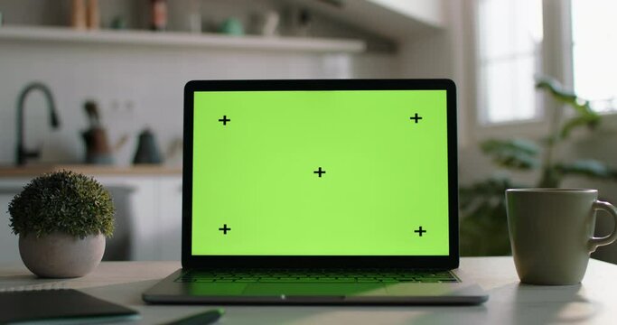 Camera moves away from green laptop screen. Chromakey on the laptop screen, green screen on the laptop display on the kitchen table. Work from home, remote work. Template with a green laptop screen