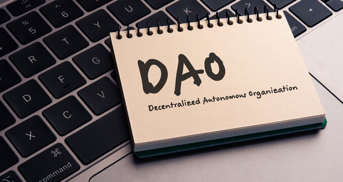 There is note book with the word Decentralized Autonomous Organization on a laptop. It is an eye-catching image.