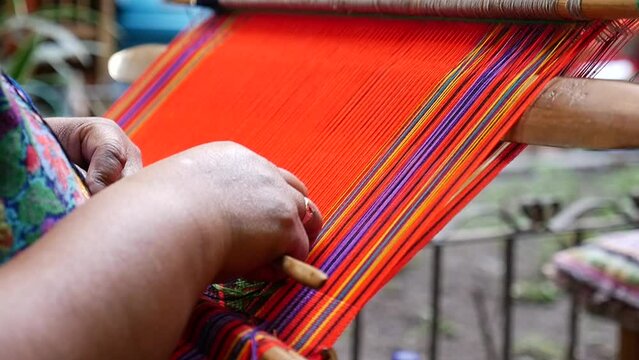 Guatemalan woman's hands weaving red string into colorful textile in market in Antigua