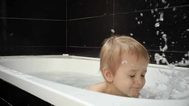 Cute smiling baby boy having fun playing in the bath with sponge, water and foam. The picture represents the joy and excitement of bath time for babies.