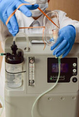 Hands in medical gloves hold out an oxygen mask against the background of the oxygen generator concentrator to deliver at low lung oxygen saturation for Covid-19 pneumonia. Focus on oxygen mask