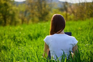 woman with laptop sitting with her back to the camera in a field
