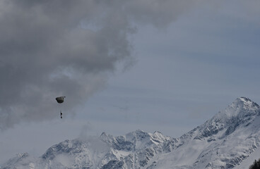 View of snow covered mountains in the Swiss alps, with landing Army paraglider in full gear