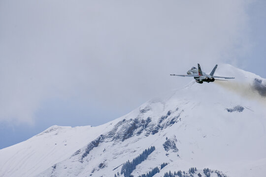 Fighter jet after take of in Swiss alps - snow covered mountains with FA18 - lots of white space, overcast, clouds