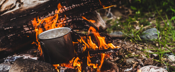 Kettle stands on fire. Cooking food at fire in wild. Beautiful big log burns in bonfire close-up....
