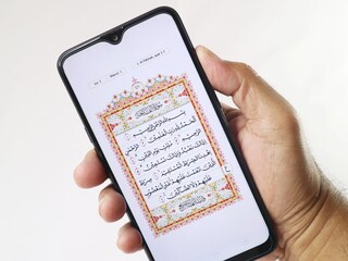 Hand holding mobile phone showing Quran application at surah Al-Fatihah