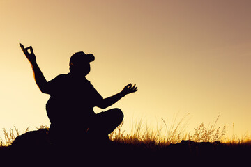 the silhouette of a man in a cap sitting in the lotus position and spreading his arms