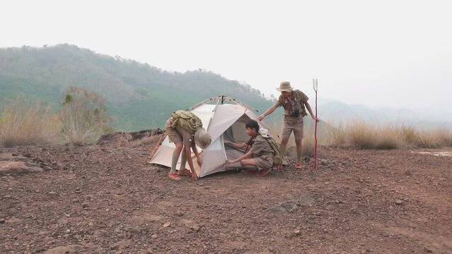 
Three Boy Scouts students attending a scout camp having good teamwork are setting up a tent to sleep in the camp in the evening as the sun sets.