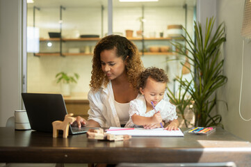 African American mother wearing casual clothes working in her home while daughter playing  or education