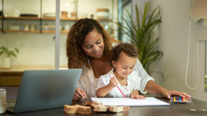 African American mother wearing casual clothes working in her home while daughter playing  or education