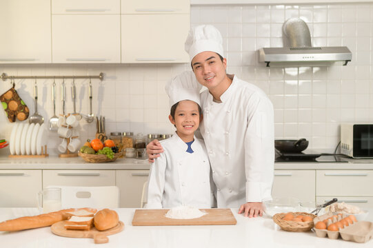 Young Asian Father And His Son Wearing Chef Uniform Baking Together In Kitchen At Home