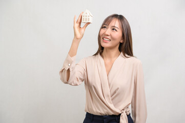 Obraz premium Young smiling woman holding small model house over white background studio.