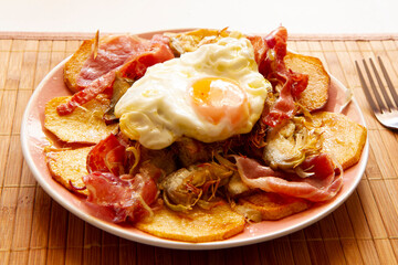 Fried eggs with chips and serrano ham. Traditional Spanish tapa nicknamed Huevos Rotos.