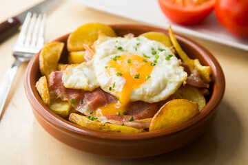 Fototapeta na wymiar Fried eggs with chips and serrano ham. Traditional Spanish tapa nicknamed Huevos Rotos.
