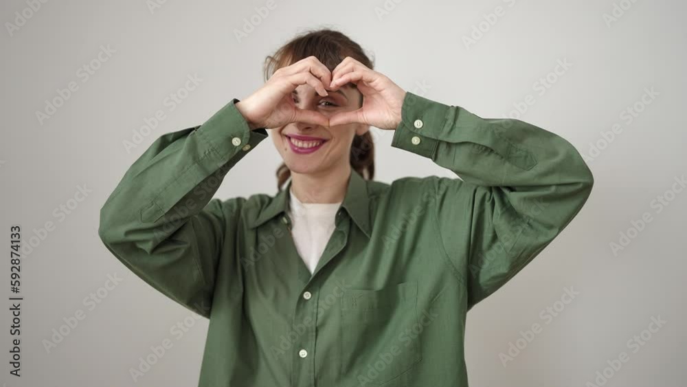 Sticker Young caucasian woman doing heart shape with hands over eye over isolated white background