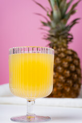 side view of a glass of pineapple juice and a pineapple on bright pink background