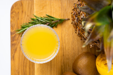 a glass of pineapple juice and a pineapple on wooden tray