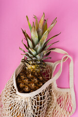 pineapple in a beige string bag on pink background