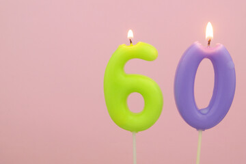 Colorful birthday candles burning and melting on pink background, numbers 60. Copy space for text.