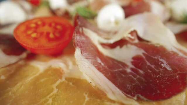 Raw ham. Slices of dried ham with rosemary, mozzarella and tomatoes. Dry-cured ham, Prosciutto Crudo