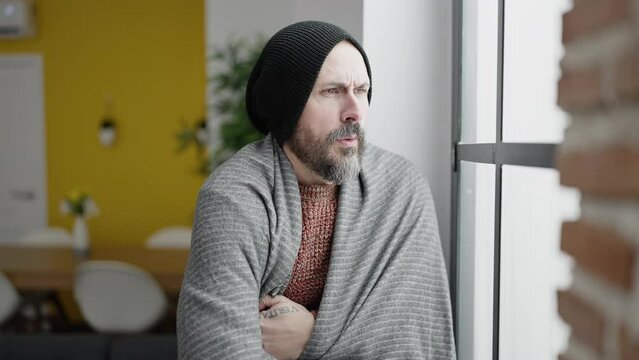 Young bald man covering with blanket looking throw the window at home