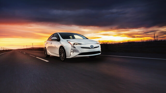 MIAMI, FLORIDA, USA - April 13, 2023 Toyota Prius XW50 white rides on the road at sunset