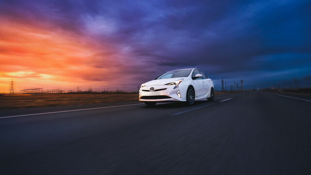 MIAMI, FLORIDA, USA - April 14, 2023 Toyota Prius XW50 white rides on the road at sunset