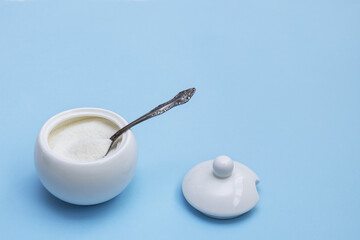 open white sugar bowl with a spoon inside and a lid next to it on a blue background with copy space