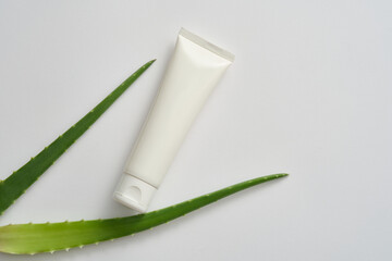 An unlabeled plastic tube and aloe vera leaves on white background. Aloe vera contains many nutrients such as antioxidants, vitamins (A, C, E) often used in cosmetics, skin care and hair care.