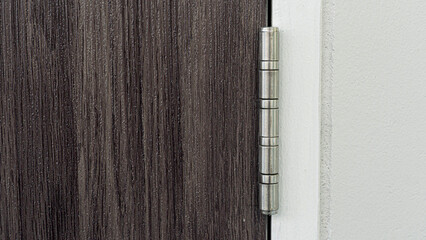 Silver-bronze door hinges with a wood-patterned door made of cherry wood and a white door frame.