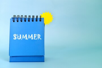 Selective focus of welcome summer reminder on desk calendar on blue background with yellow sun and copy space.