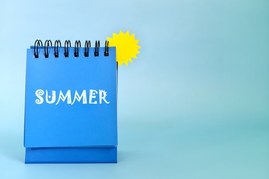 Selective focus of welcome summer reminder on desk calendar on blue background with yellow sun and copy space.