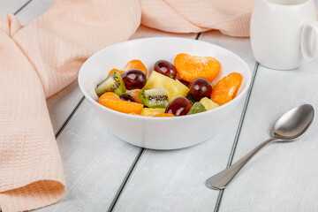 Fruit salad of pineapple, orange, kiwi and grapes in a plate on a wooden background.