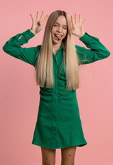 Comical funny young caucasian woman making playful silly facial expressions and grimacing, fooling around, showing tongue. Pretty crazy adult girl bullying isolated on studio pink background indoors