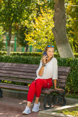 young brunette woman with a phone sits on a bench in a summer park